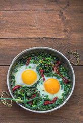 Green shakshuka. Fried eggs with fresh spinach, ramson, leek in a pan on a gray background, top view