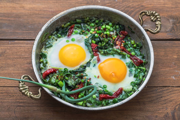 Green shakshuka. Fried eggs with fresh spinach, ramson, leek in a pan on a gray background, top view