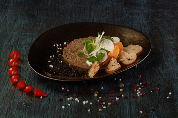 Veal tartar with red hot pepper on a beautiful dish on a background of green wood
