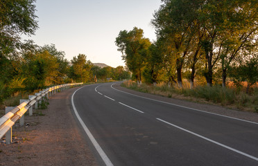 asphalt road, striped black and white road barrier in the village during sunset