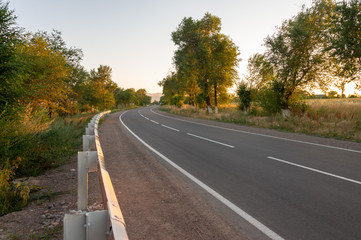 asphalt road, striped black and white road barrier in the village during sunset