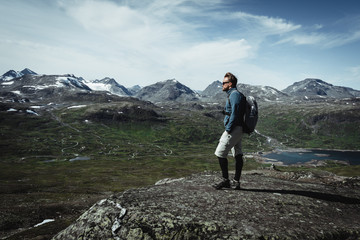 Man hiker with a backpack on the peak top enjoying the view. Concept of a feeling of accomplishment. Hiking in Jotunheimen national park Oppland, Norway. 