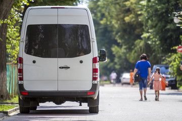 Back view white passenger medium size commercial luxury minibus van parked on summer city street.