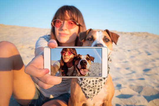 Human taking a selfie with dog. Best friends concept: young female makes self portrait with her puppy outdoors on a beach