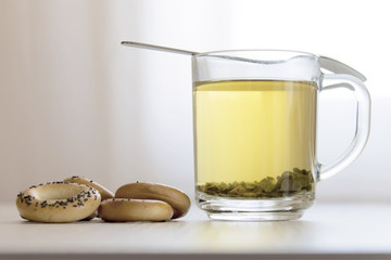 Transparent cup of green tea and bagels lying on light wooden table.