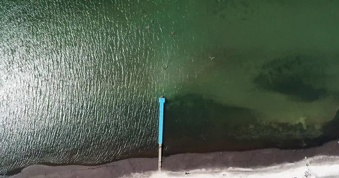 Video loop with aerial footage showing bird eye view with people walking and getting tan on a tropical Florida beach under blue umbrellas and turquoise ocean waves breaking against the coastal line