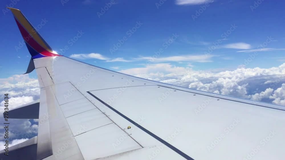 Poster view from plane window of the left wing of plane with clouds in the background and blue sky. travel 