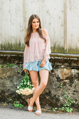 Happy beautiful woman with soft white roses, wearing blush cold shoulder blouse and denim shorts