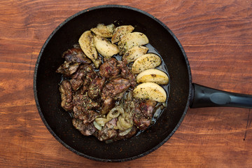 Fried chicken liver with onion and stewed apples in metal pan, wooden background.