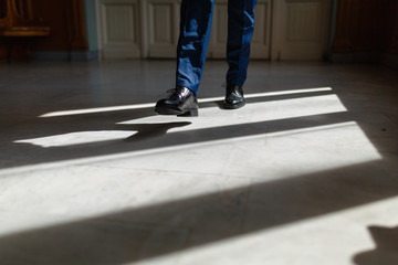 Legs of a man in an expensive suit and black shoes during a step. A person walks along the corridor of the living room or hotel marble floor under the sunlight. Legs close up. Business concept