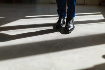 Fototapeta na wymiar Legs of a man in an expensive suit and black shoes during a step. A person walks along the corridor of the living room or hotel marble floor under the sunlight. Legs close up. Business concept