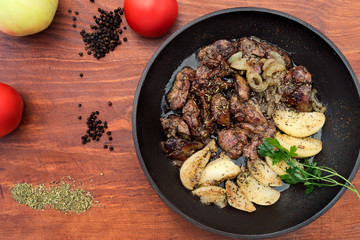 Fried chicken liver, stewed apple slices, whole tomatoes, spices of dry herbs, black pepper, all on a wooden background, top view.