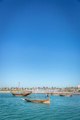 Fototapeta na wymiar Traditional boat in a blue water sea with some buildings in the background in a blue sky day in Doha, Qatar