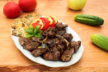Chicken liver stewed with apples and onions, decorated with basil, tomato and pepper slices, wooden background.
