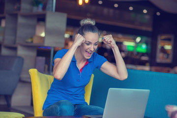 Winner girl euphoric watching a laptop in a coffee shop wearing a blue shirt