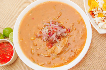 Above view of traditional Ecuadorian food called Encebollado, fish stew and ring onions inside, served with popcorn, chifles, lemon and red sauce inside of bowl