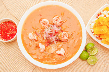 Above view of Ecuadorian food: shrimp cebiche with some chifles inside white bowl, lemon and red spicy salad inside a white bowl in a wooden table background