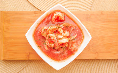 Above view of delicious traditional ecuadorian shrimp cebiche in rectangular white bowl served over a wooden structure in table background