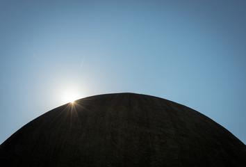 Fototapeta na wymiar The sun breaking over the edge of a silhouetted dome, appearing like the sun over a distant planet