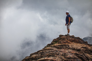 A man standing on a rugged rocky peak amongst moody clouds