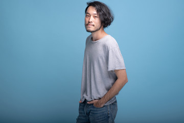 Young bearded man hands in pocket in blue background.