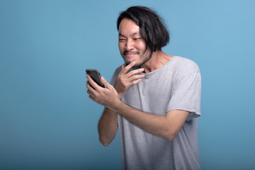 Fototapeta premium Excited Young bearded man looking at mobile message in blue background.