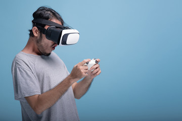 Young bearded man playing VR game in blue background.