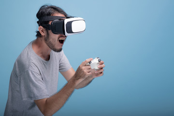 Young bearded man playing VR game in blue background.