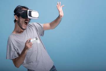 Young bearded man playing VR game in blue background.