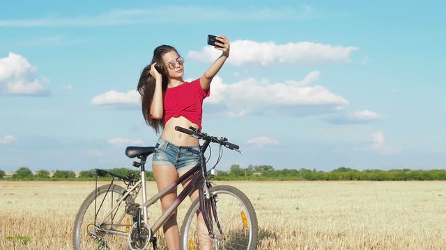 The girl makes selfie. A sporty girl with a bicycle takes a picture of herself on the phone.