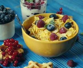 Healthy breakfast with corn flakes, berries, waffle and milk on blue background.