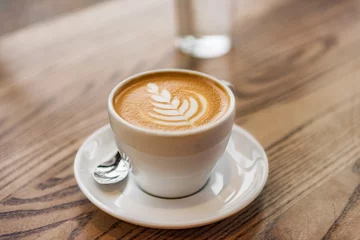 Fototapeten Latte Art in Cappuccino-Kaffeetasse am Café-Tisch. Nahaufnahme der Rosetta-Blumenzeichnung im Schaum. © Maridav