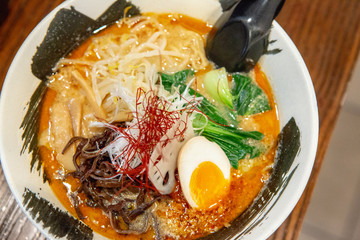Bowl of Japanese tantanmen ramen noodles soup with ground pork, egg, bok choy, on a wooden table.