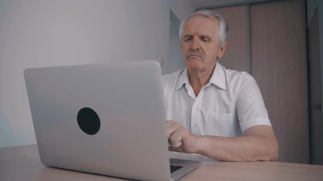 Gray-haired Senior man with mustache working at laptop in office sitting at table