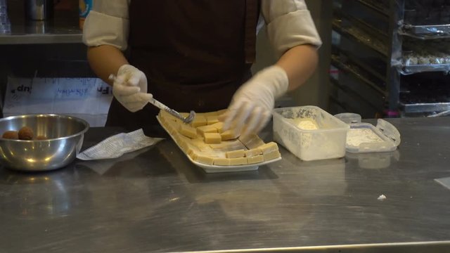 Woman made white chocolate powder falls sifting on chocolate bars and arrange down the dish
