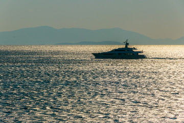 Motor yacht at sea at sunrise. In the background the silhouette of the mountains.