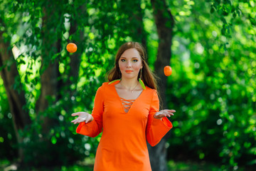 Portrait of pretty red hair woman throwing up two delicious mandarins at summer green park.