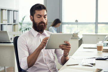 Handsome bearded businessman reading data on digital tablet