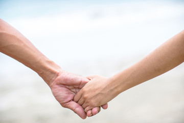 Summer couple holding hands at sunset on beach. Romantic young couple enjoying sun, sunshine, romance and love by the sea. Couple on summer vacation travel holiday.