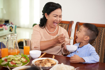 Grandmother feeding her little grandson at dinner table