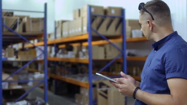 Inspector use tablet in warehouse at blurred background of shelves with products