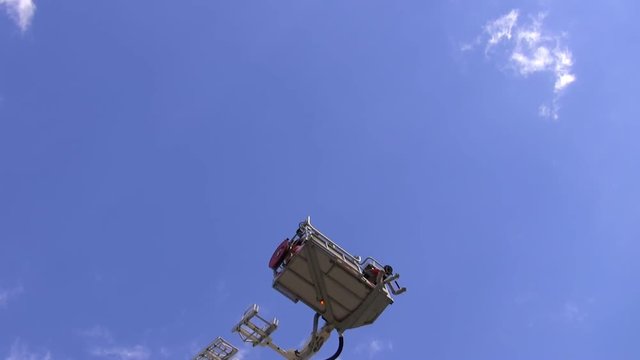 Telescopic firefighters aerial ladder platform is raising with people in it. Blue sky background