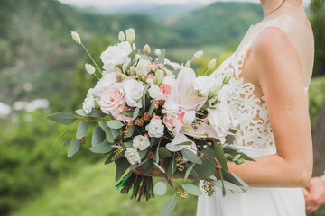 Bride holding gentle wedding bouquet with lily, pink roses and greens in hands
