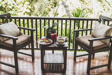 Breakfast outdoor on wooden terrace with jungle view. Eggs, fresh watermelon juice and orchid flower on table