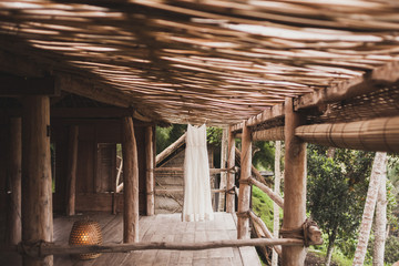 Fototapeta na wymiar White wedding dress hanging in tropical bamboo house in morning. Bride getting ready