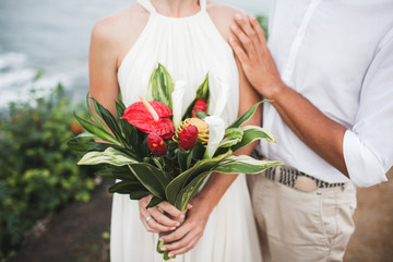 Bouquet with red and green tropical flowers in bride's hands