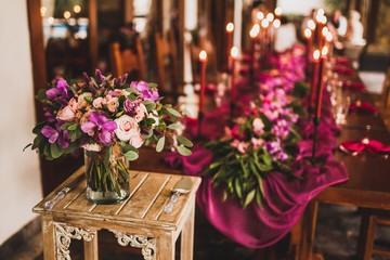 Wooden wedding table decorated with red candles, pink cloth and purple orchids. Romantic family dinner in evening