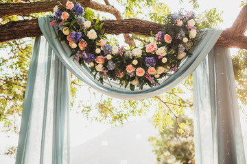 Sunset wedding ceremony, arch decorated with grey cloth hanging on big tree and rose flowers...