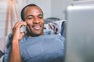 Comfortable conditions. Relaxed man working on the laptop while speaking on the phone