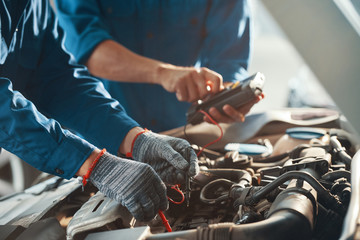 Mechanics using multimeter when checking work of car engine in garage